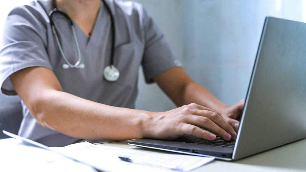 Doctor with stethoscope working on laptop